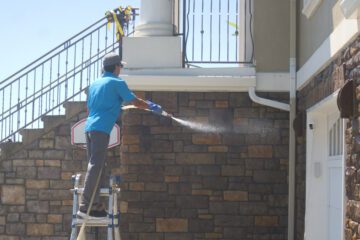 Johnny Tsunami technician using soft wash equipment to clean the siding of a residential home.